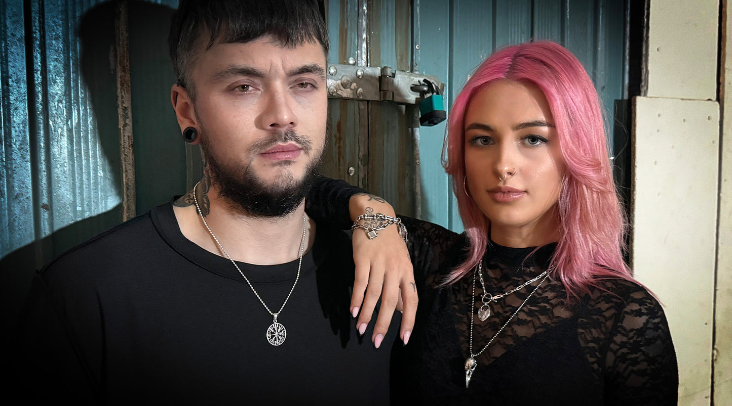 Layered silver jewellery from ROCKSTAR★REFINEMENTS, including the RECKLESS ROUTE, ACCESS DENIED, and CROW'D CONTROL pendants with coordinating wrist chains, styled against an industrial backdrop.