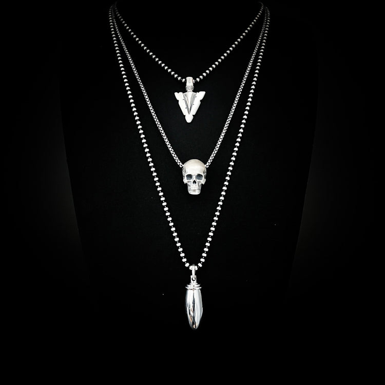 Silver layered necklaces with final point arrow pendant, resting dead face skull pendant, and pretty loaded vial locket. 