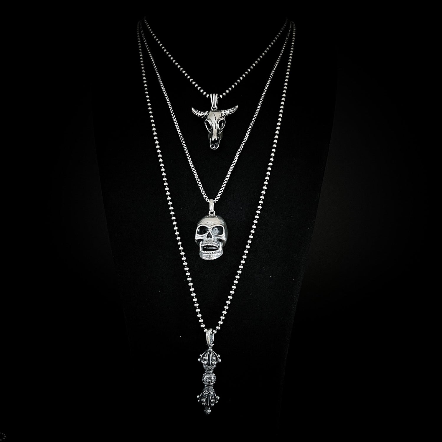 Layered chains from the ROCKSTAR★REFINEMENTS HARDER: FOR HIM collection — featuring NO BS, FINAL LAUGH, and the WARBORN RELIC pendants on oxidised chains against a black background. 