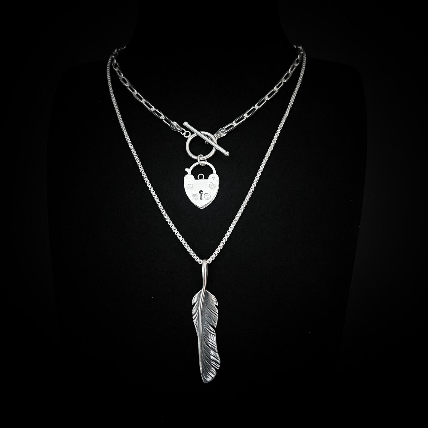 ACCESS DENIED padlock pendant and PLUCK OFF feather pendant from the EXES & EXCUSES collection by ROCKSTAR★REFINEMENTS, styled together on layered silver chains against a black background.