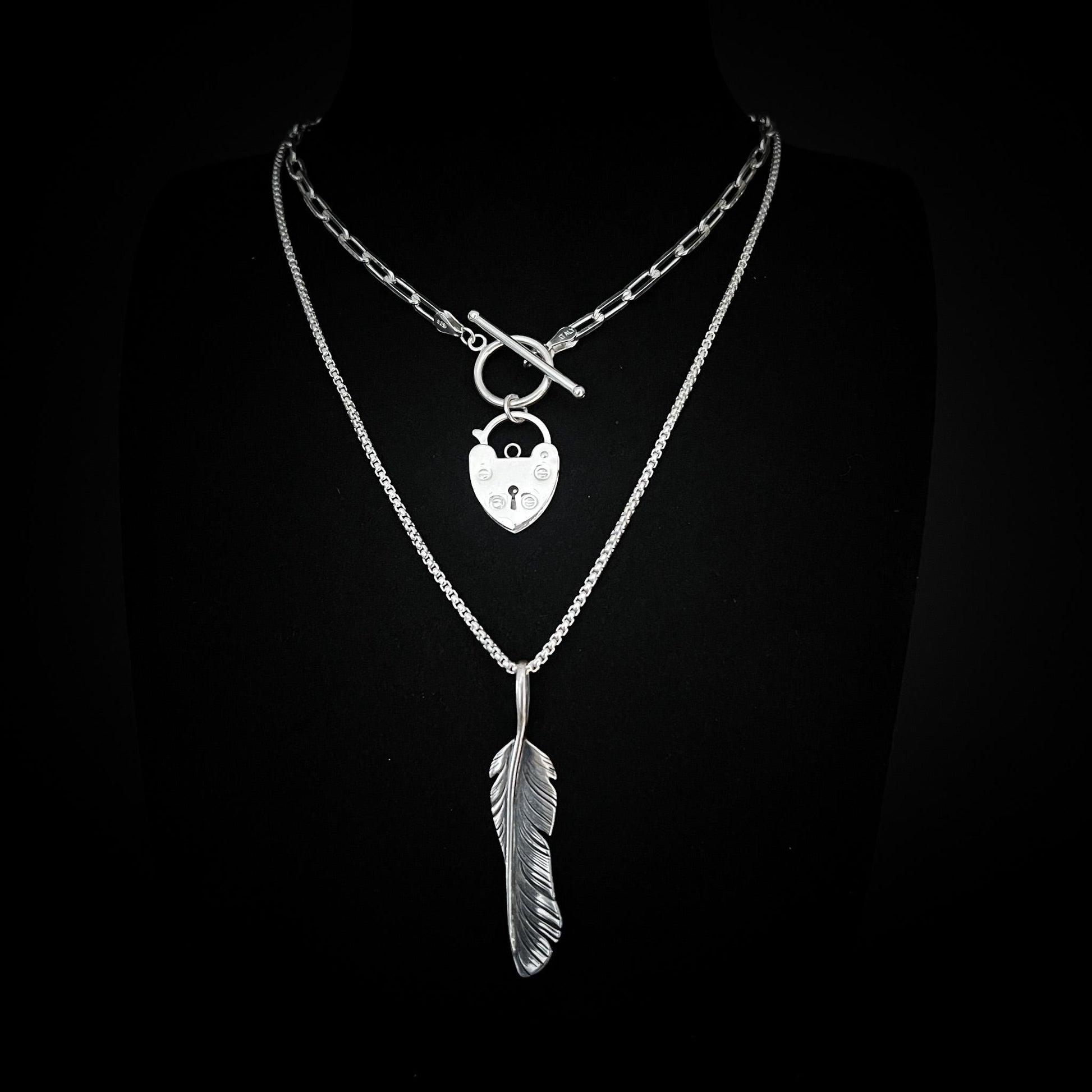 ACCESS DENIED padlock pendant and PLUCK OFF feather pendant from the EXES & EXCUSES collection by ROCKSTAR★REFINEMENTS, styled together on layered silver chains against a black background.