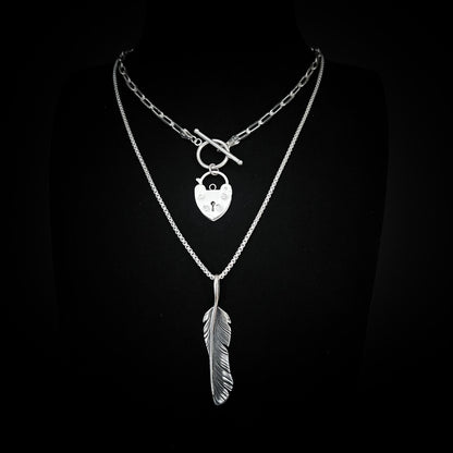 ACCESS DENIED padlock pendant and PLUCK OFF feather pendant from the EXES & EXCUSES collection by ROCKSTAR★REFINEMENTS, styled together on layered silver chains against a black background.