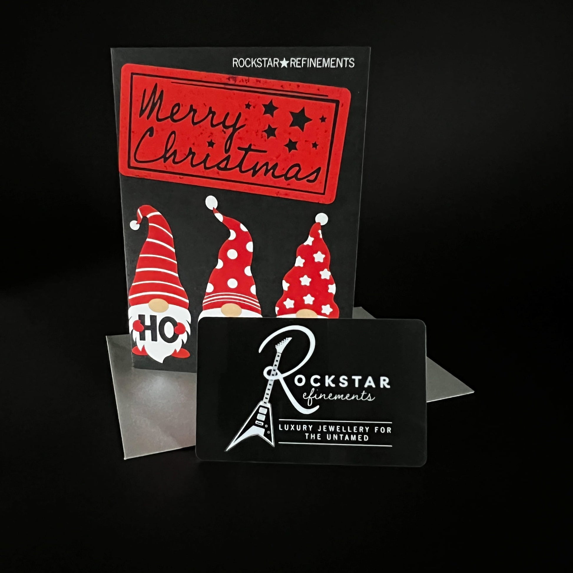 Ho Ho Ho Christmas card and silver metallic envelope with a physical ROCKSTAR★REFINEMENTS gift voucher card, photographed on a black background.
