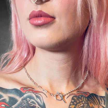 Close-up of a person with pink hair and tattoos wearing the CROSSFADE necklace by ROCKSTAR★REFINEMENTS™