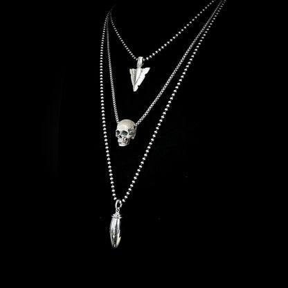 DEADLY LITTLE DEATAILS collection featuring FINAL POINT arrowhead, RESTING DEAD FACE skull and PRETTY LOADED pendants in sterling silver, on a black background.