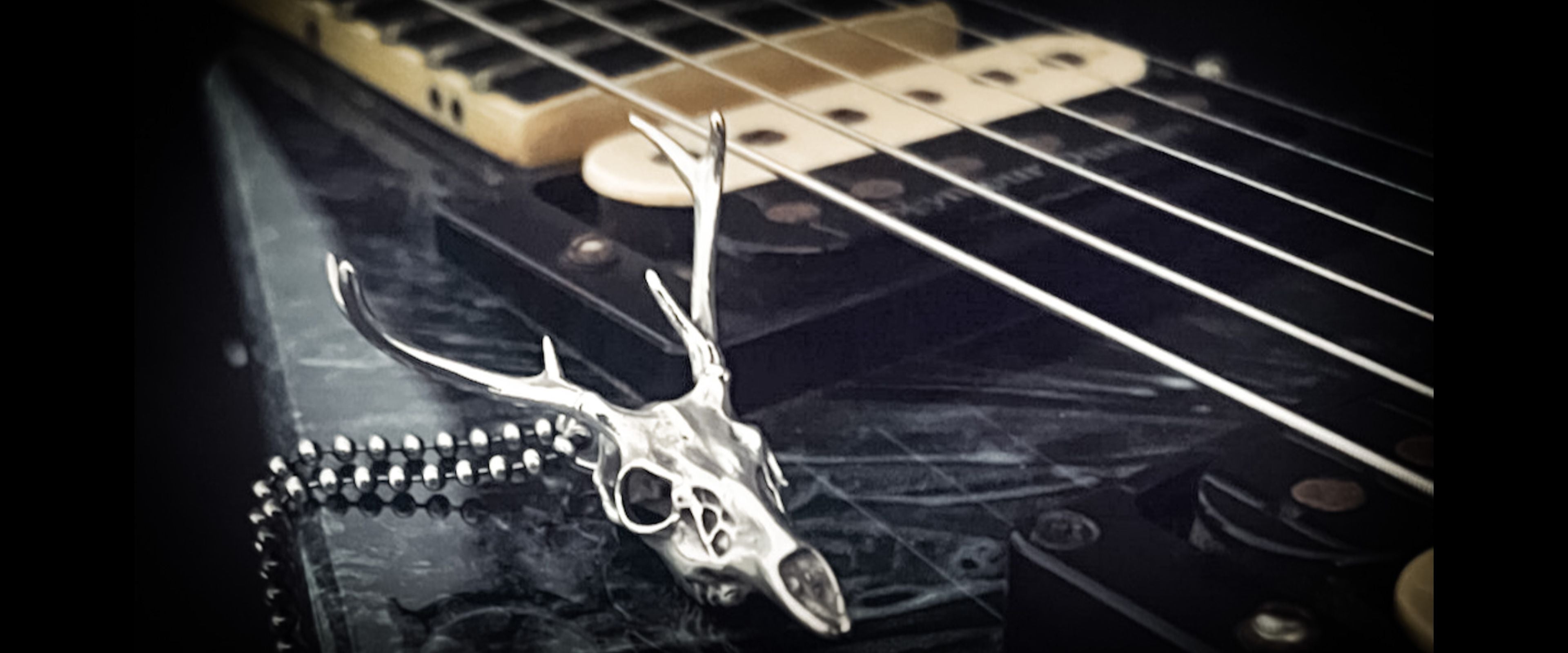 Sterling silver FAWN OF THE DEAD sterling silver deer skull pendant by  ROCKSTAR★REFINEMENTS displayed on an Jackson V electric guitar.
