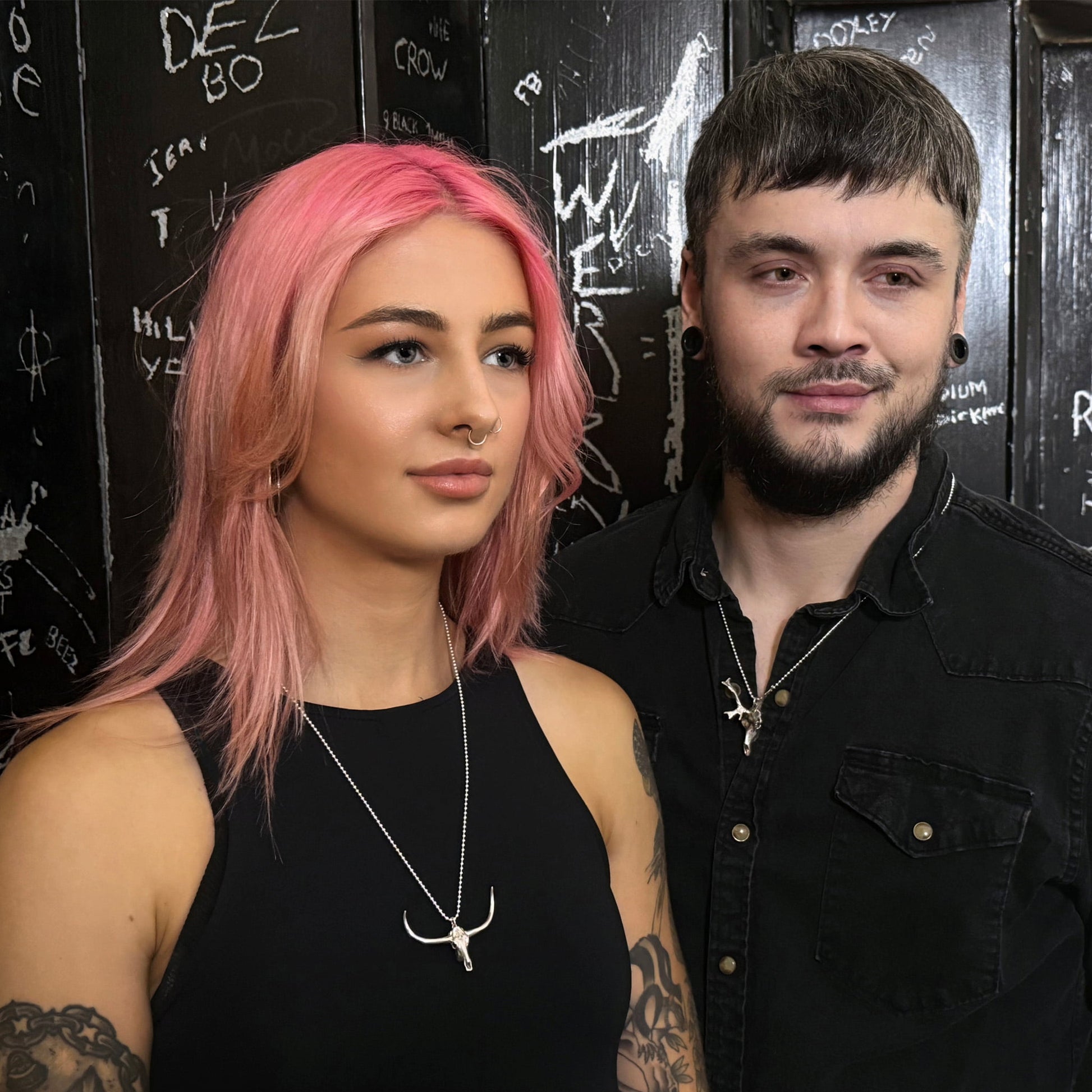 Model on the left wearing DON'T SQUAT WITH YER SPURS ON pendant on a 24" ball chain next to model on the right wearing the HORNOGRAHY on a 24" ball chain