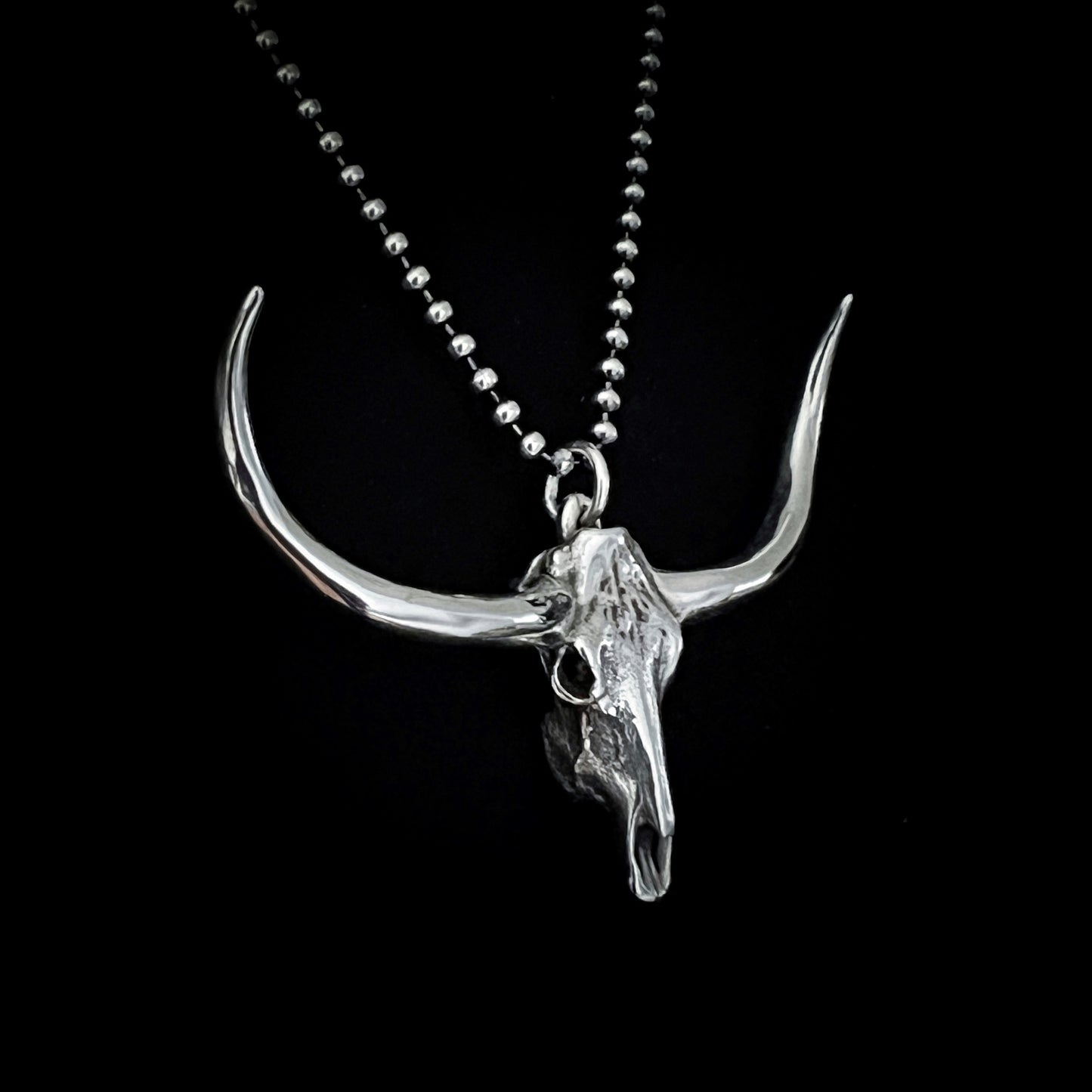 DON'T SQUAT WITH YER SPURS ON sterling silver pendant shown close-up on 24-inch oxidised ball chain, on black background