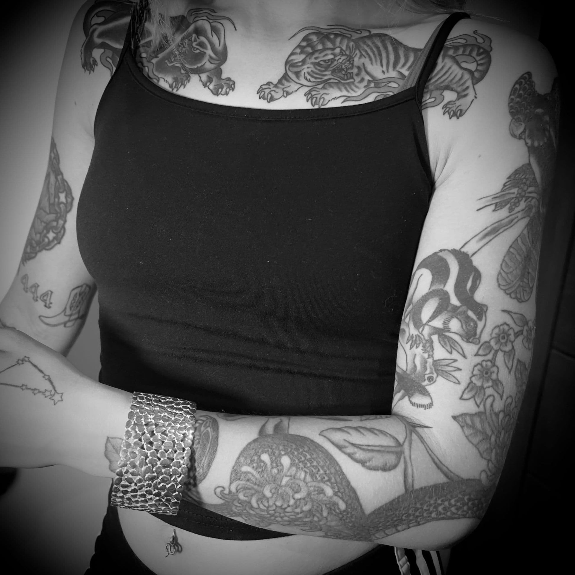 Black & White photo of a person wearing a black vest top with visible tattoos on arms and chest wearing MAINSTAGE bangle by ROCKSTAR★REFINEMENTS™