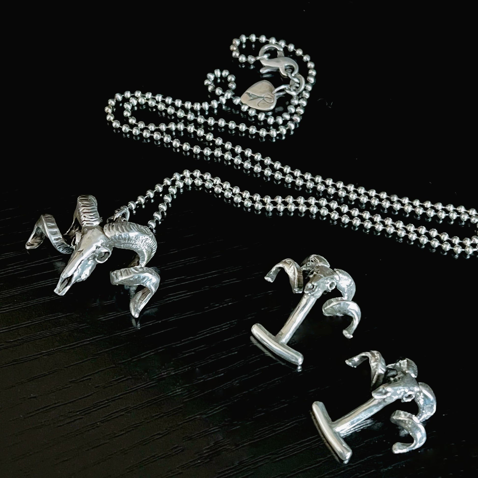 NO FLOCKS GIVEN pendant on oxidised ball chain, and FLOCKING FORMAL cufflinks photographed on a black background 