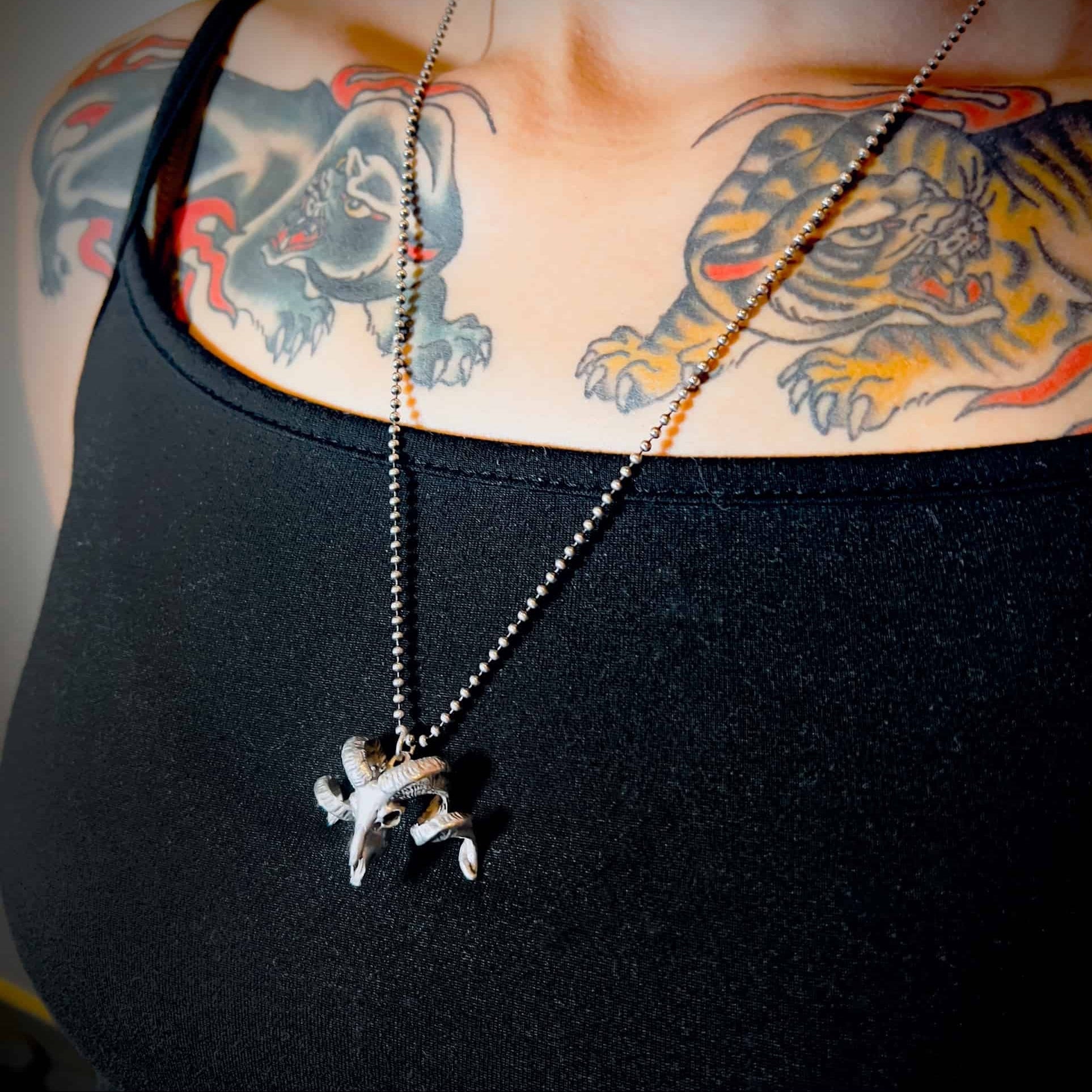 NO FLOCKS GIVEN solid silver pendant on ball chain, worn by tattooed person