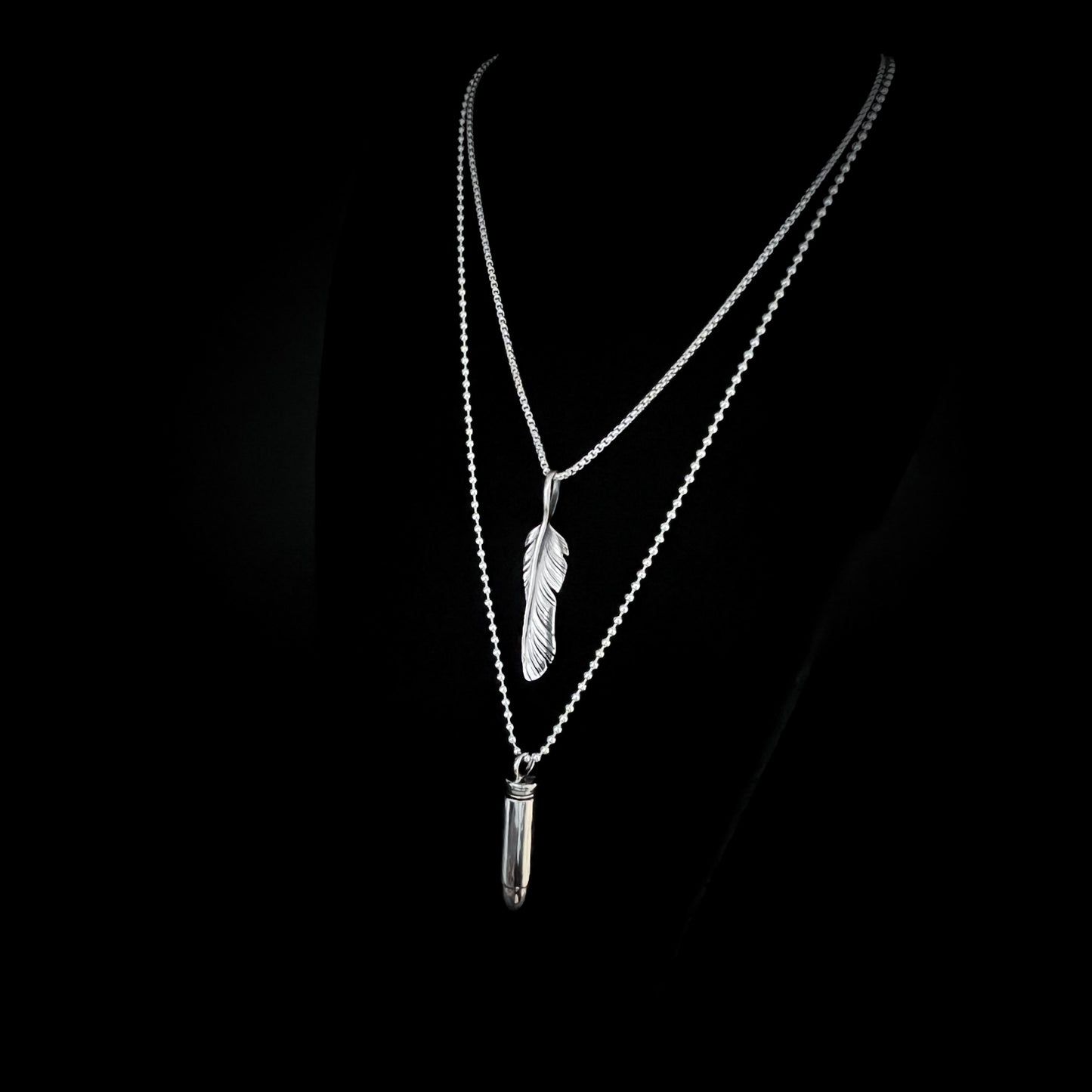 THE ONE STEP COOL KIT — sterling silver layered necklaces featuring WINGING IT on a 26-inch box chain and ONE HIT WONDER bullet pendant on a 30-inch 2.5 mm ball chain, photographed on a black background, side view, by ROCKSTAR★REFINEMENTS