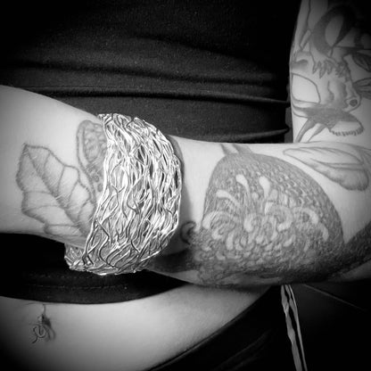 Close-up of a person's arm with tattoos wearing PRETTY TWISTED sterling silver bangle by ROCKSTAR★REFINEMENTS™