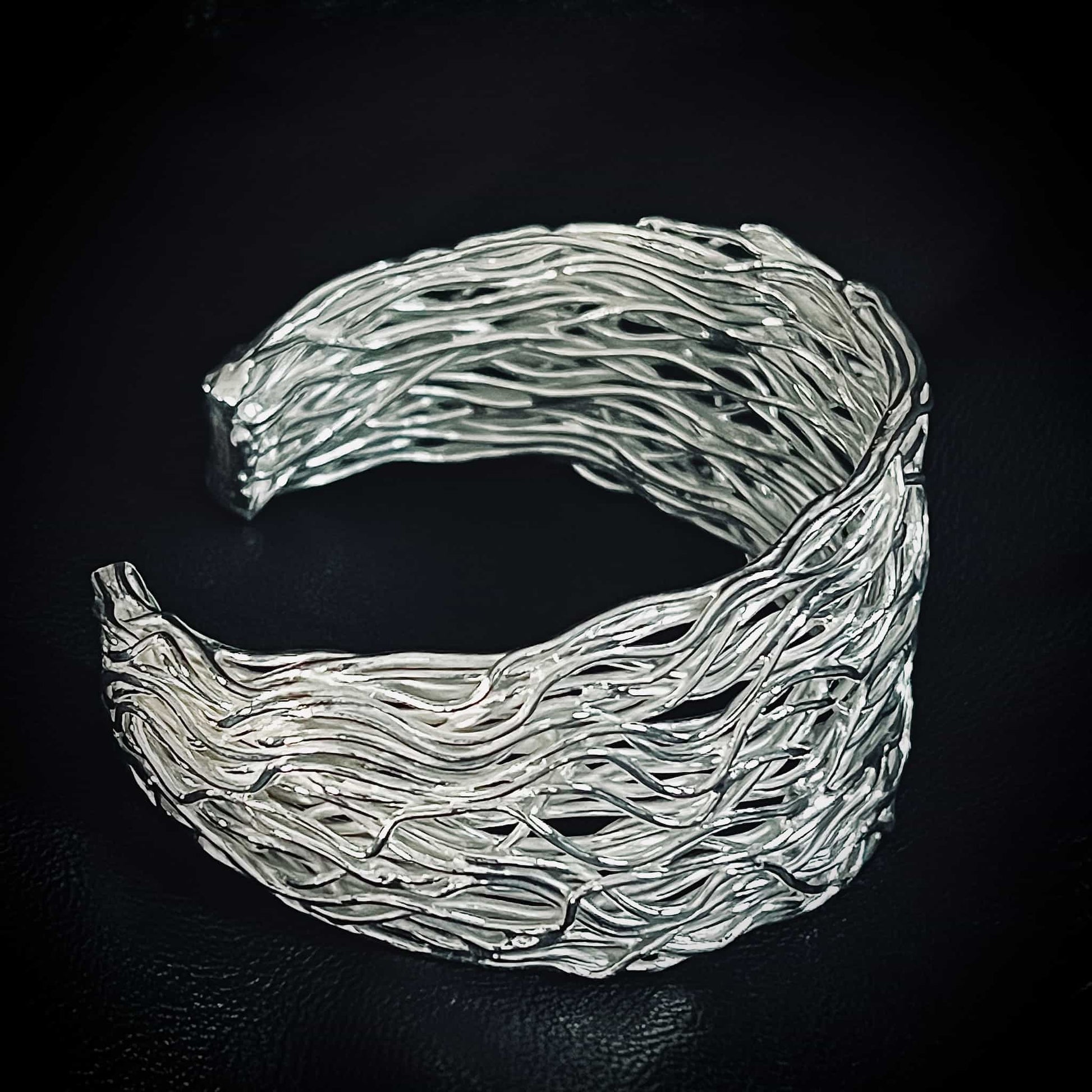 PRETTY TWISTED iconic sterling silver statement bangle by ROCKSTAR★REFINEMENTS™. Photographed close-up from a side-view on a black background. 