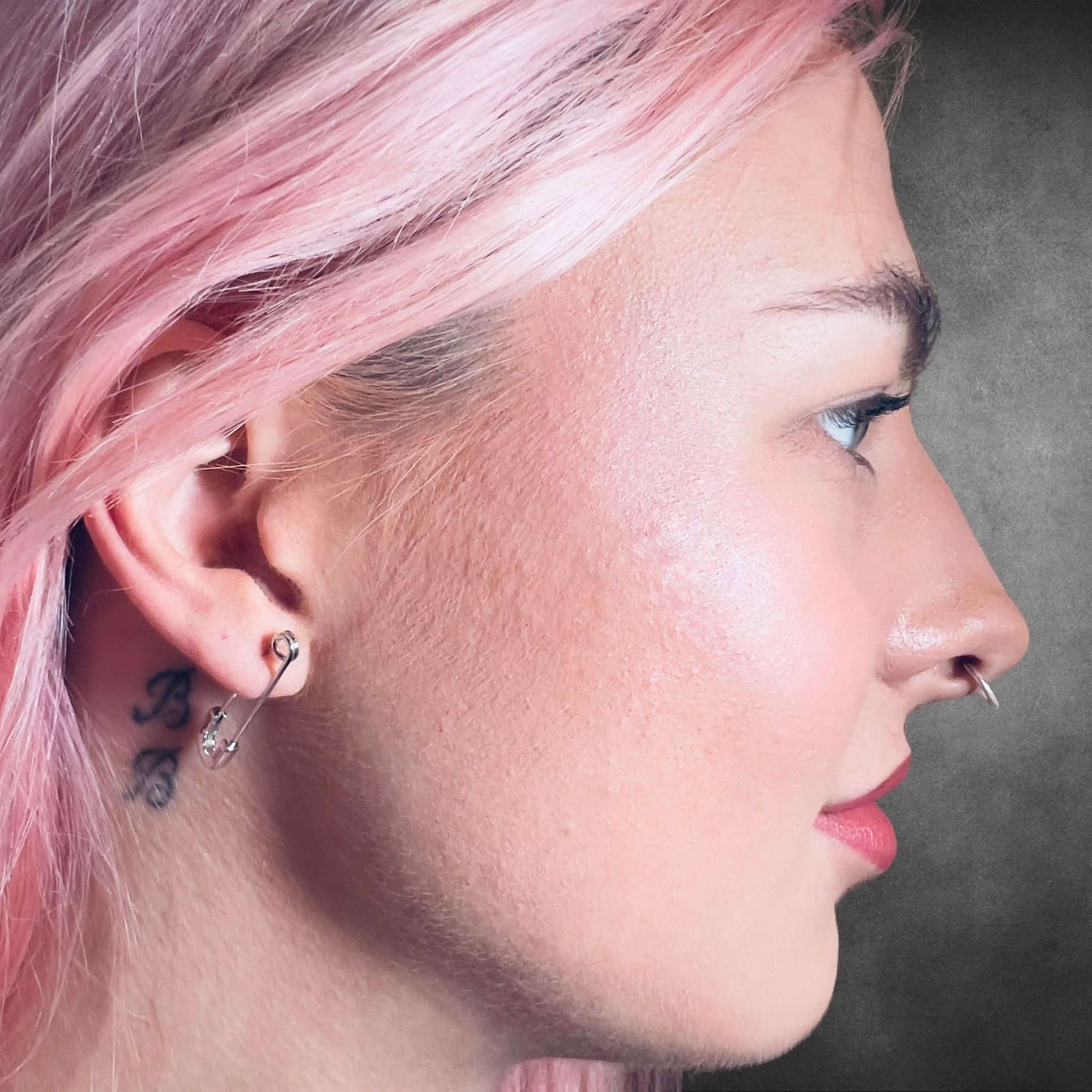 Pink-haired model wearing sterling silver SAFETY LAST earrings by ROCKSTAR★REFINEMENTS™ in side profile close-up.