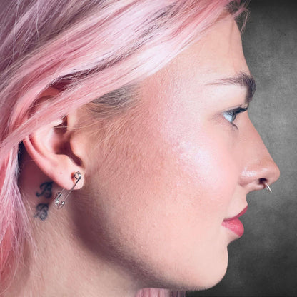 Pink-haired model wearing sterling silver SAFETY LAST earrings by ROCKSTAR★REFINEMENTS™ in side profile close-up.