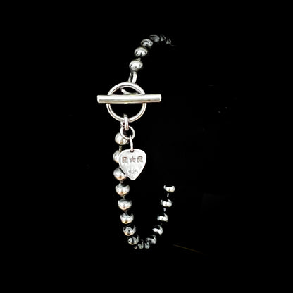 SIDEKICK SLAYER oxidised bracelet photographed on black background. With toggle and bar clasp and ROCKSTAR★REFINEMENTS™ guitar pick shaped branded jewellery tag.