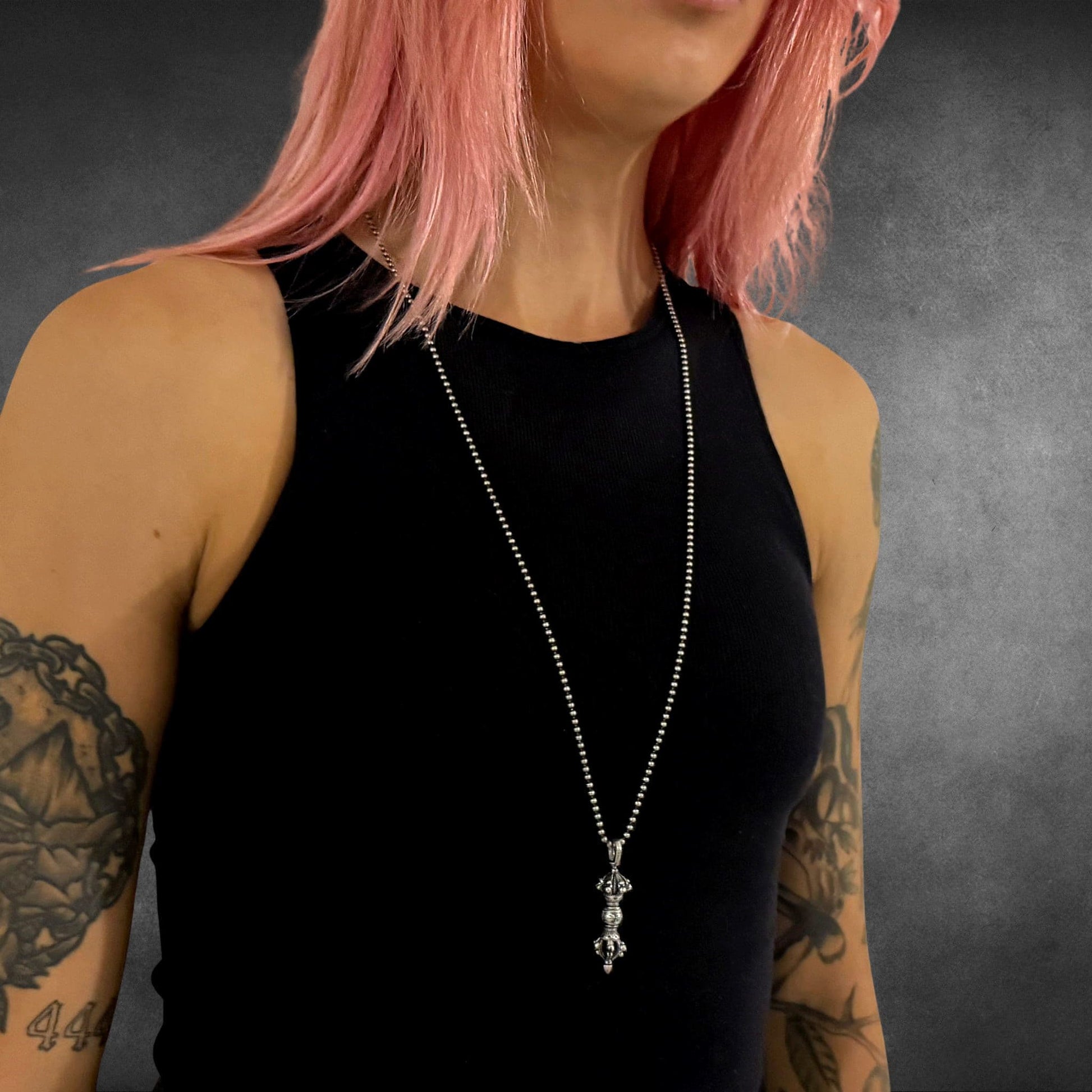 Tattooed person wearing the WARBORN RELIC on 30-inch ball chain against a dark background