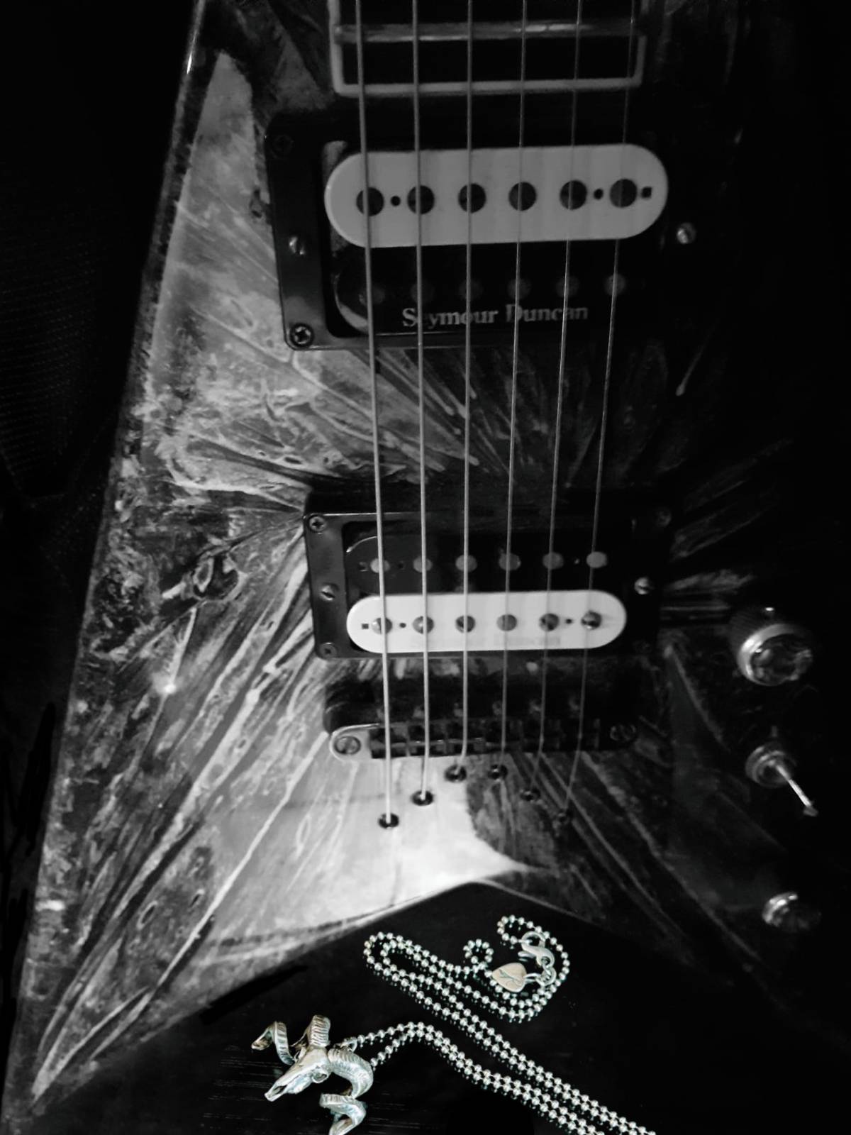 Sterling Silver NO FLOCKS GIVEN pendant in front of a Jackson V guitar— reflecting  ROCKSTAR★REFINEMENTS
heavy-metal roots and luxury edge