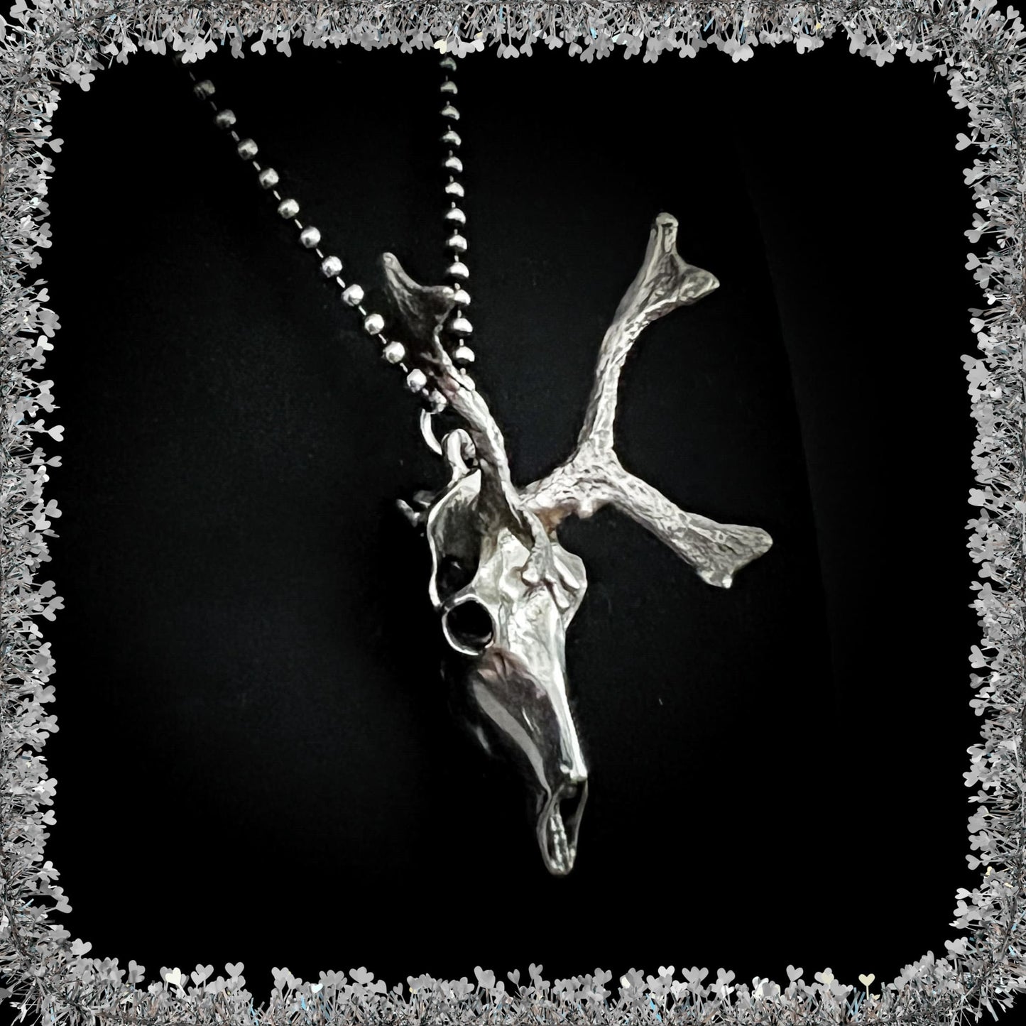 Sterling silver reindeer skull pendant on a 24 inch ball chain against a black background with a tinsel border